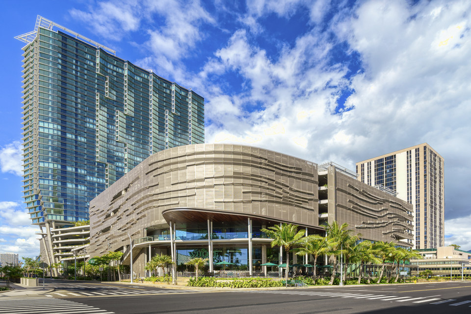Contemporary glass tower and sculptural urban podium under a dramatic Honolulu sky.