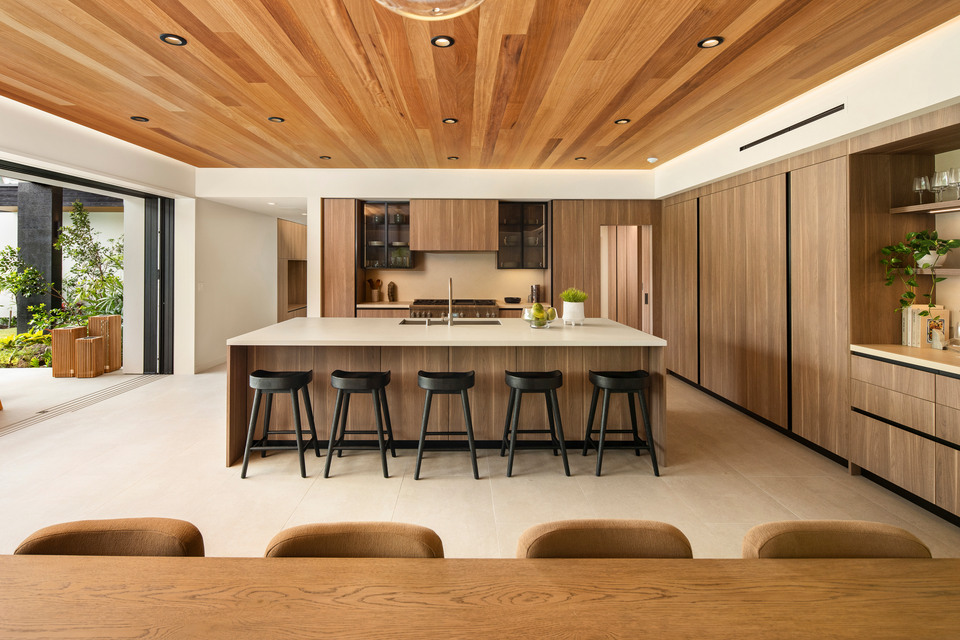 Kitchen interior with a central island, wood cabinetry and an opening to a garden.