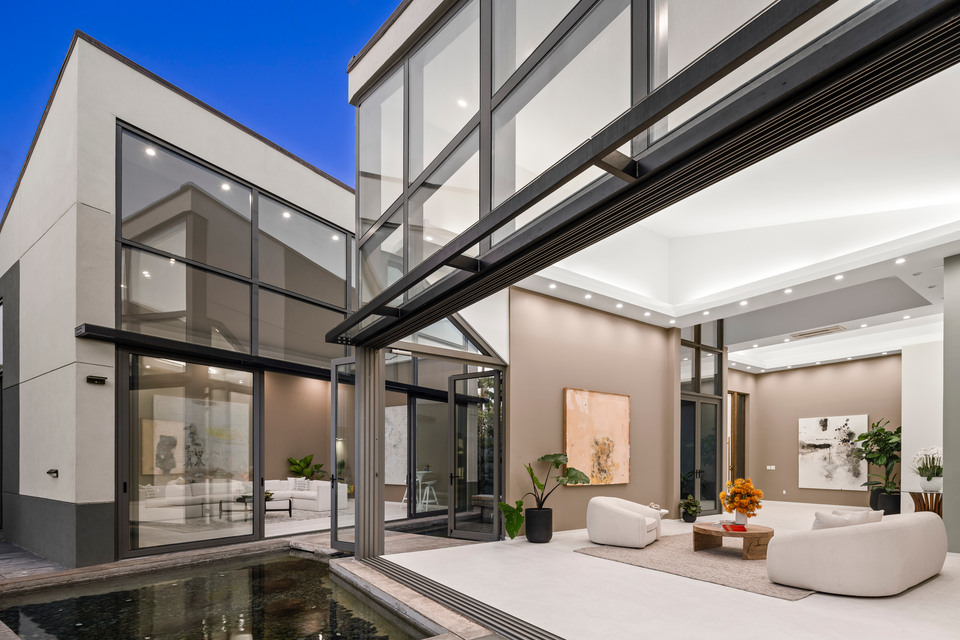 Modern glass-walled residence with an illuminated interior at dusk.