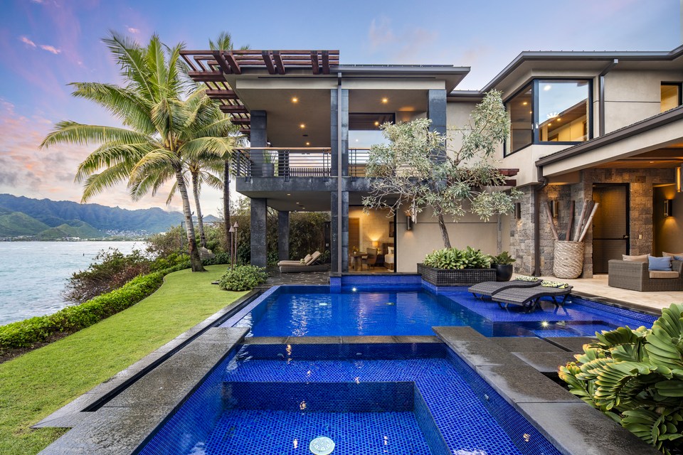 Contemporary façade and pool framed by palm trees at twilight.