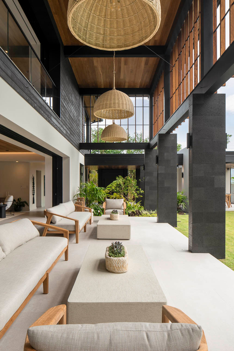 Double-height covered living space with woven pendant lights and garden views.