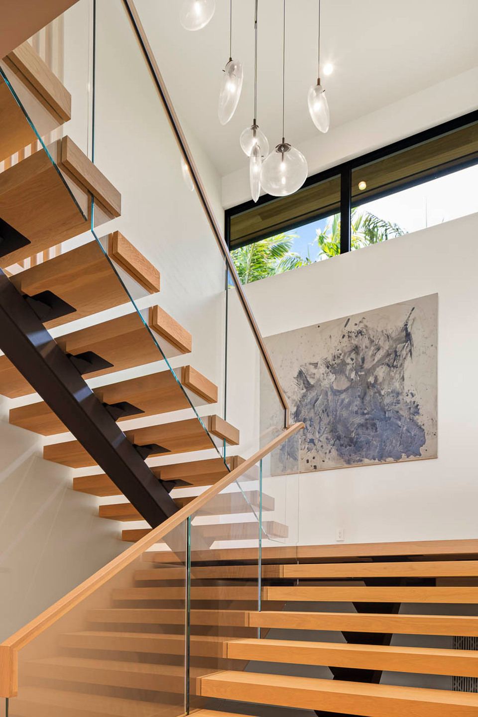 Open-riser wood staircase beneath a cluster of glass pendant lights.