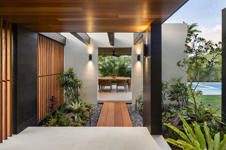 Sheltered entry walkway with wood soffits and layered tropical landscaping.