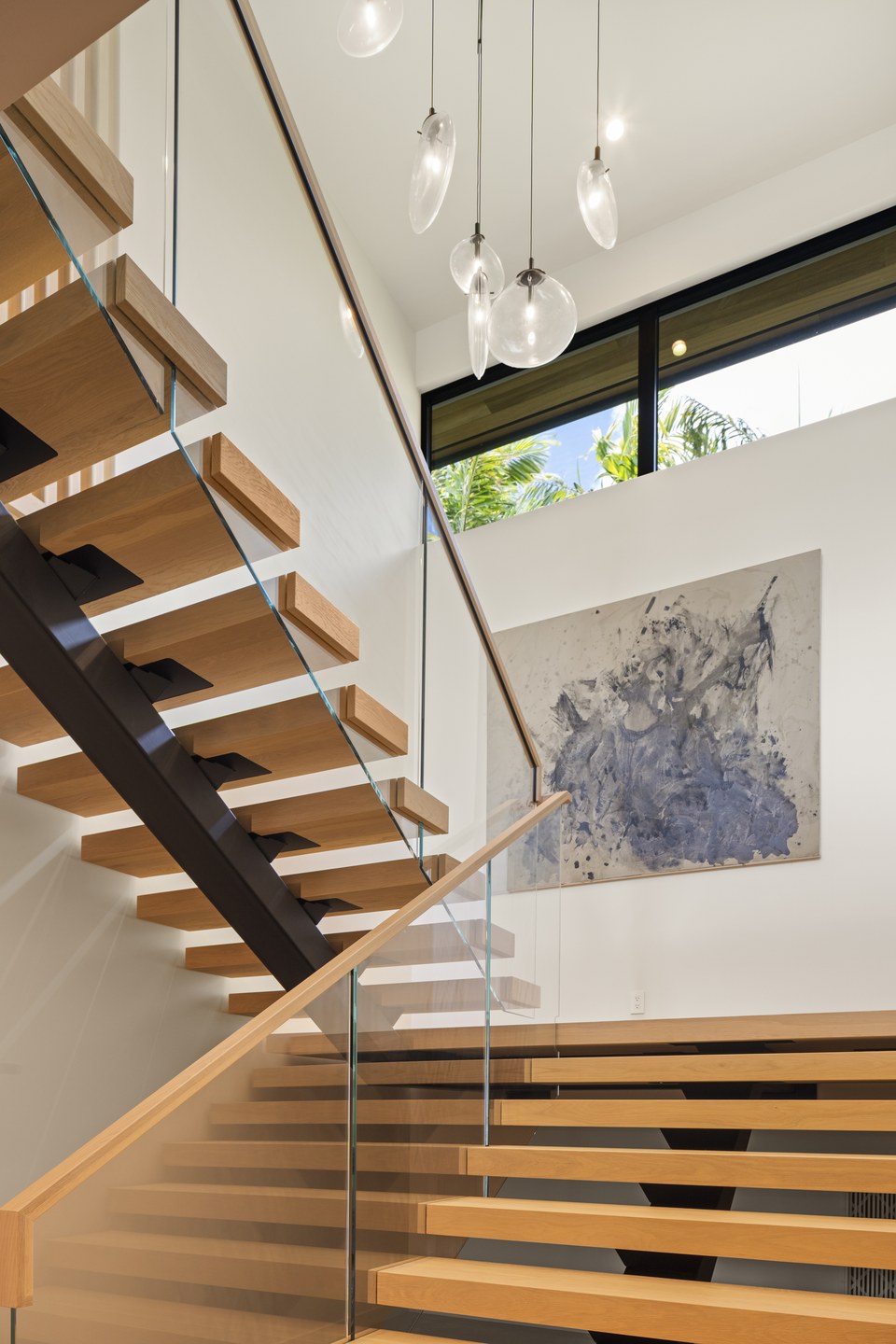 Open-riser timber staircase beneath a cluster of glass pendant lights.