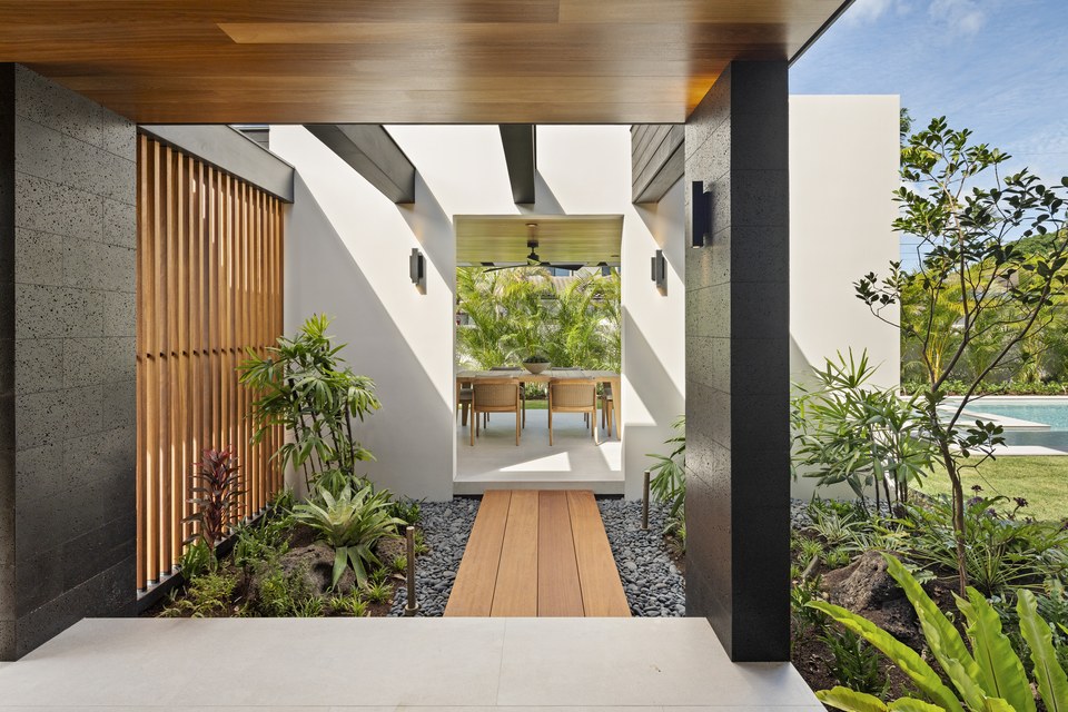 Covered entry passage framed by dark stone, warm timber and tropical planting.