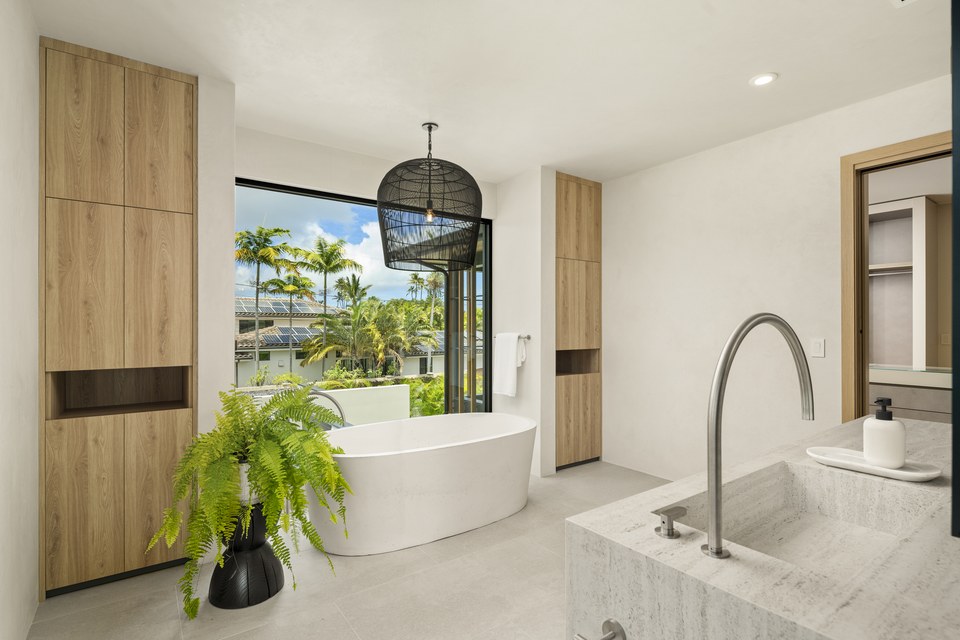 Primary bathroom with a freestanding tub, pale timber cabinetry and tropical views.