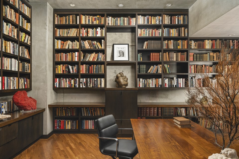 Custom library with dark shelving, warm wood and collected objects.