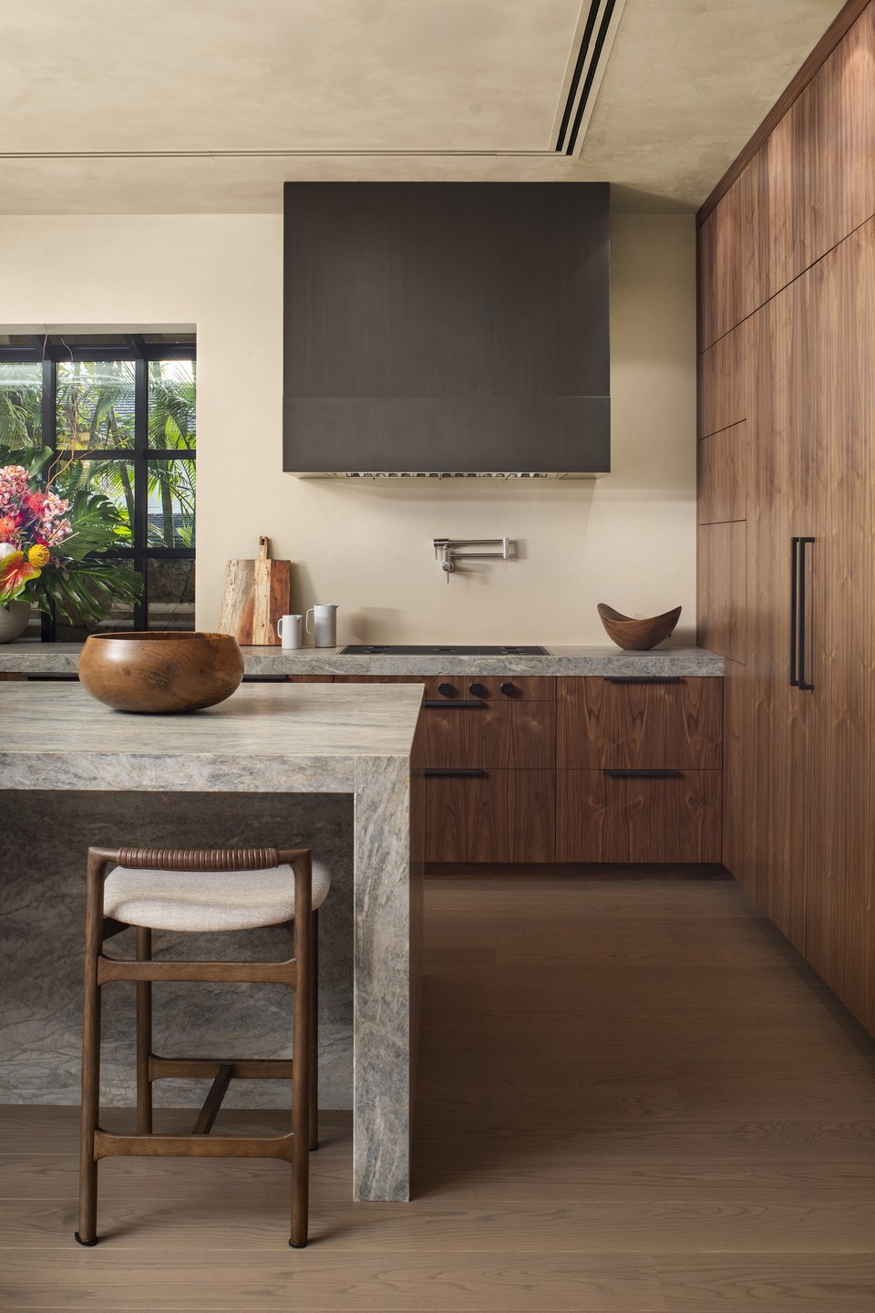 Walnut kitchen with stone surfaces, tailored cabinetry and a garden view.