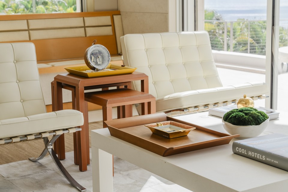 Sunlit Hawaiʻi lounge with white leather seating, tailored nesting tables and an ocean view.