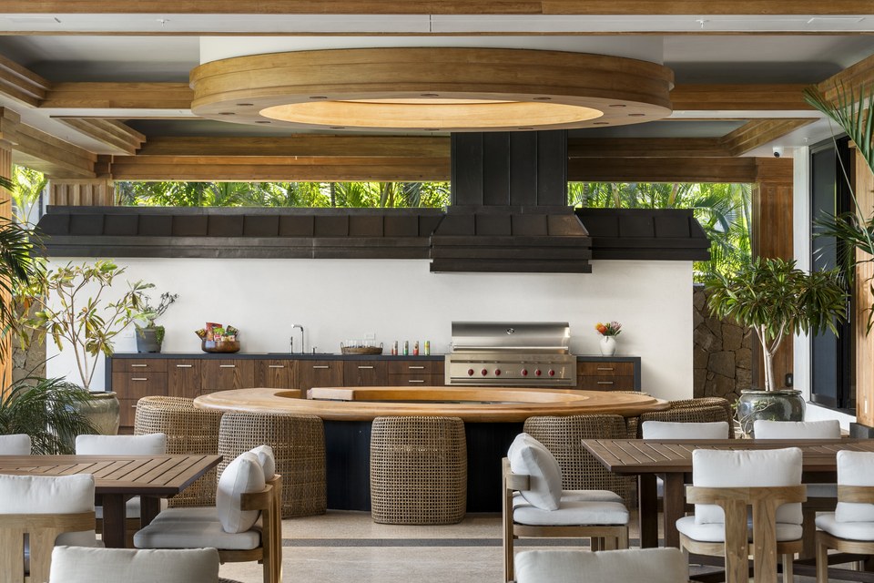 Designed outdoor kitchen and dining pavilion with layered woodwork, woven seating and tropical landscaping.